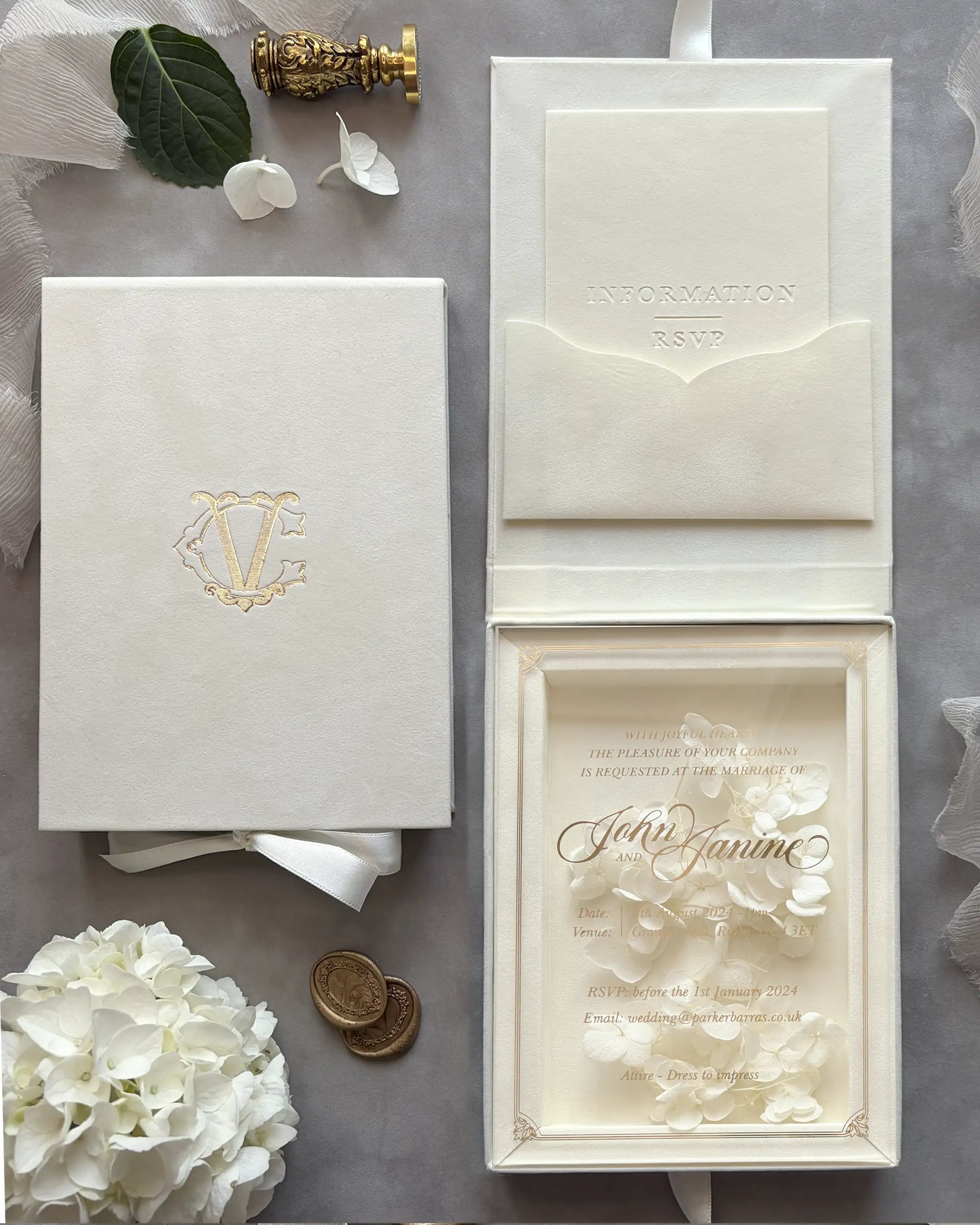 Cream velvet boxed wedding invitation suite featuring a custom gold foil monogram on the lid and a clear acrylic invitation card adorned with delicate white hydrangeas — Polina Perri